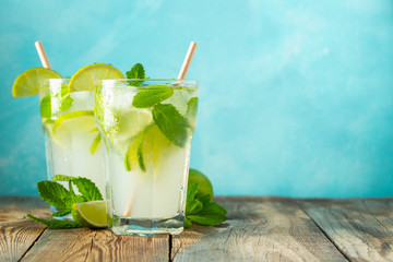 Two homemade lemonade or mojito cocktail with lime, mint and ice cubes in a glass on a wooden rustic table. Fresh summer drink. With copy space.