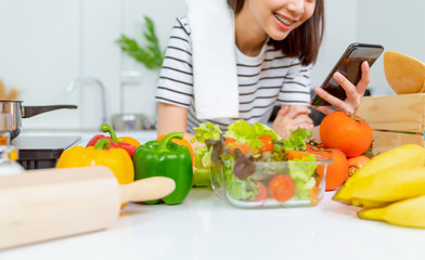 Obraz na płótnie Canvas Woman hand holding a smartphone and salad bowl with tomato and various green leafy vegetables on the table at the home, take your advertising.