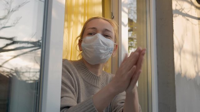 Woman in protective mask on the face looking in through the open window applauds