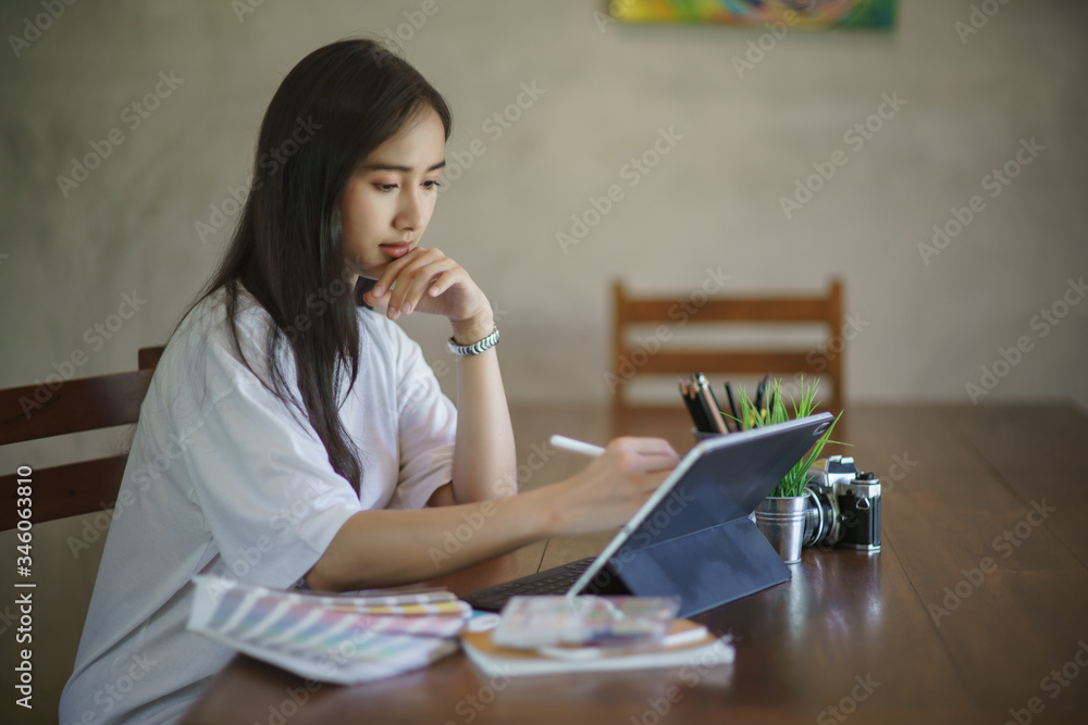 Poster young asian female designer using graphics tablet while working with computer at home.
