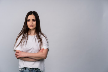 Young girl in white shirt on gray background, she expresses the emotion of resentment and brooding