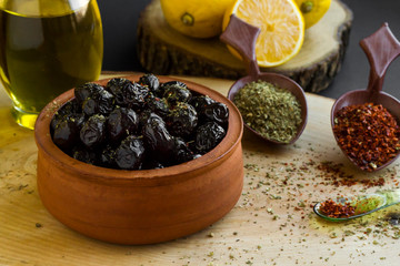 Black olives marinated with seasoning in caserolle bowl on wood block with lemon,seasoning and olive oil bottle.