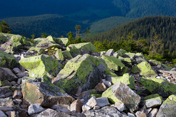 Huge stones covered with green lichen on top of a mountain against the backdrop of mountains and...