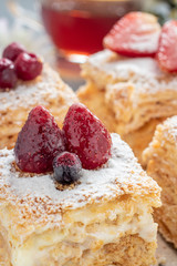 Delicious layer cake Napoleon decorated with berries and powdered sugar on a gray stone Board on a gray-yellow background, vertically
