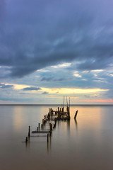 Obraz premium Morning scenery with rain clouds in the sky and golden light from the sun at a fishing village with an old, broken wooden bridge.