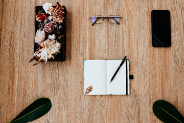 Flat lay, top view of a notepad with white paper and pen for planning an upcoming trip, or freelancer plan. Smartphone to view the route. glasses near the notebook,Seashells