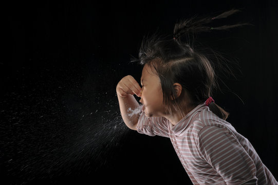 Kid Of Sneezing, Coughing, Shocking Food Concept. A Little Asian Girl Of 7 Years Old Covered Nose While Sneezing And Causing The Water To Flow Out Of The Mouth With Black Background.