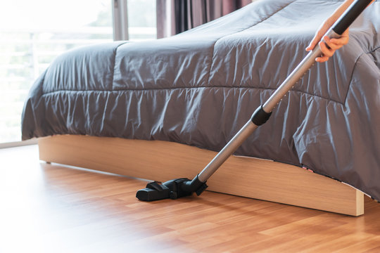 Woman cleaning the bedroom in her house by using a vacuum.