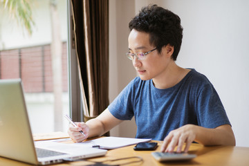 Young Asian businessman in relax casual during working from home. Asian man staying at home and setup a small workplace during COVID-19 self isolation. Work from home concept during coronavirus crisis