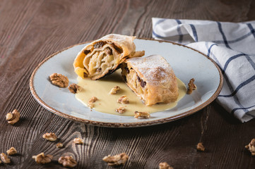 Traditional piece of apple strudel with powdered sugar on wooden table