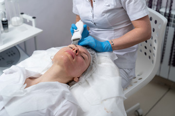 Beautician does facial skin cleansing for his client. Cleansing the skin with special tools. Facial cleansing mask.