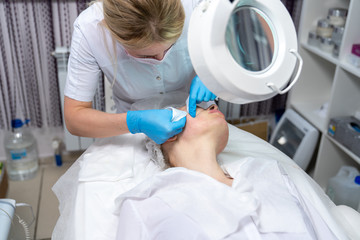 Beautician does facial skin cleansing for his client. Cleansing the skin with special tools. Facial cleansing mask.