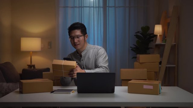 Asian entrepreneur man working and checking order online at computer and scan code via phone at home. Work from Home overload at night, self isolation in new normal concept.Working late and Overtime