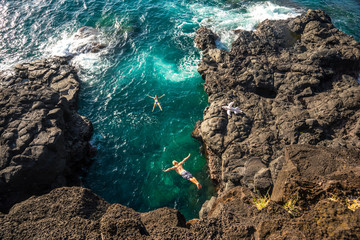 Young muscular guy jumping from a high cliff into the clear ocean on the island of Mauritius. Girl...