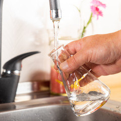 A man pours tap water into a glass flask.