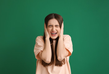 Young woman suffering from loud noise on color background
