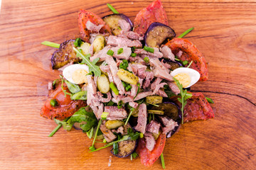 Salad with tufts of beef meat, grilled eggplant and tomatoes, arugula and egg on a wooden board,...