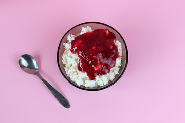 Top view of a bowl with cottage cheese and a glass jar with fresh raspberry jam, accompanied by a spoon. Copy space - the concept of proper nutrition, benefits, natural products