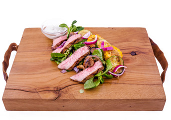 Salad with beef slices, grilled vegetables - eggplant, corn, mushrooms, sauce on a wooden board, dish. The object is isolated on a white background.