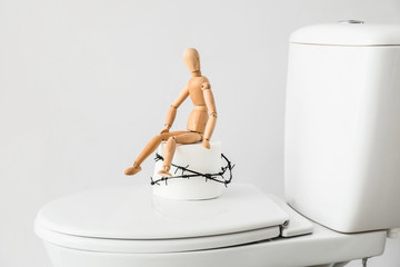 Toilet bowl with roll of paper, barbed wire and wooden human figure on light background....