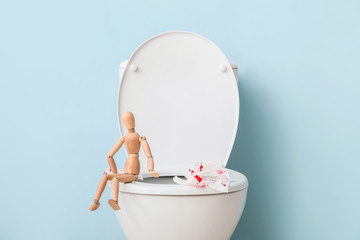 Toilet bowl, wooden human figure and paper with blood spots in restroom. Hemorrhoids concept