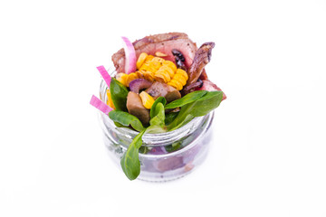 Salad with pieces of beef meat, grilled vegetables - eggplant, corn, mushrooms, sauce in a glass jar on a white background