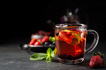 Fruit red tea with berries in glass cup on black background