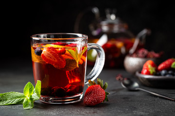 Fruit red tea with berries in glass cup on black background