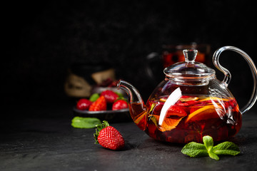 Fruit red tea with berries in glass teapot on black background