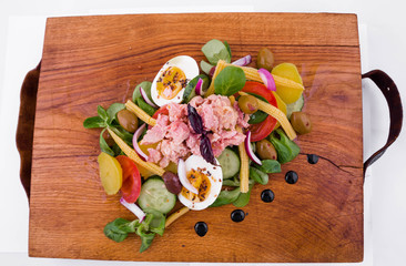Salad with tuna, fresh vegetables - cucumber and tomatoes, canned corn, boiled potatoes, herbs, onions, olives on a wooden tray, board, dish. The object is isolated on a white background.