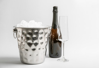 Bucket with ice, bottle of champagne and glass on light background