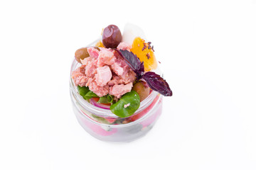 Nicoise salad with tuna, vegetables, olives and capers in a glass jar on a white background