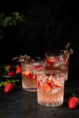 Refreshing summer drink with strawberry slices in glasses on black background