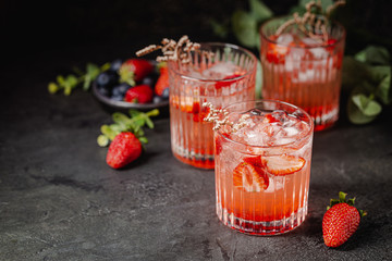 Refreshing summer drink with strawberry slices in glasses on black background