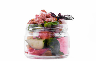 Nicoise salad with tuna, vegetables, olives and capers in a glass jar on a white background