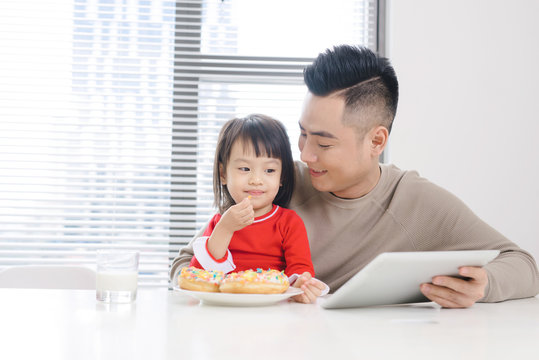 Young Asian Dad And Daughter Eating Pizza While Watching On Ipad.