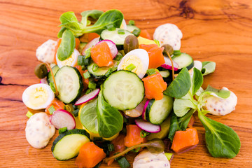 Salad with red fish, fresh vegetables - cucumber and radish, capers, egg, herbs, olives and sauce on a wooden tray, board, dish.