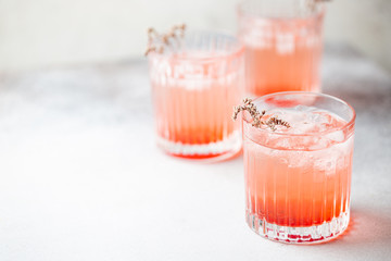 Cold fresh pink lemonade drink with ice in a glass on white background, selective focus