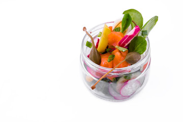 Salad with red fish, fresh vegetables - cucumber and radish, capers, egg, herbs, olives in a glass jar. The object is isolated on a white background.