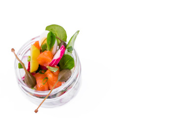 Salad with red fish, fresh vegetables - cucumber and radish, capers, egg, herbs, olives in a glass jar. The object is isolated on a white background.