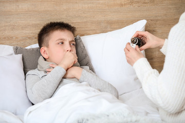Mother giving medicine to her son ill with flu at home