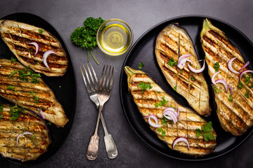 Grilled eggplant slices, garnished with fresh herbs, on black background, top view