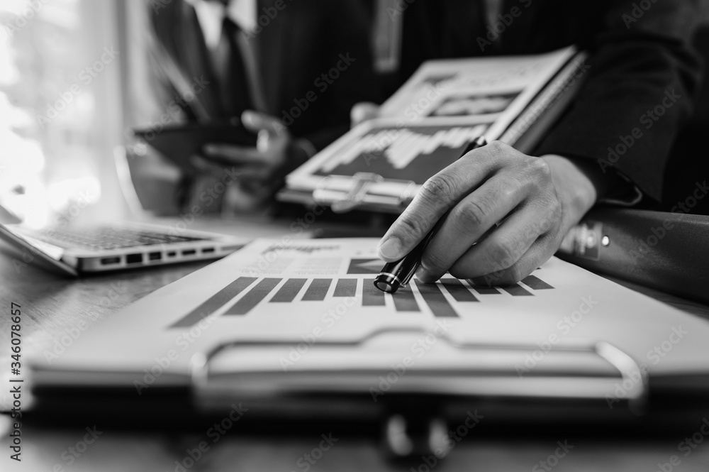Poster business documents on office table with smart phone and laptop and two colleagues discussing data in
