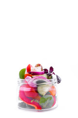 Greek salad with feta cheese, blue onion and..pesto sauce in a glass jar on a white background