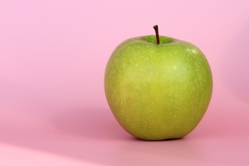 Green yellow apple on a pink background. Juicy ripe beautiful fruit.