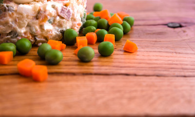 Olivier salad with shrimp, pickled cucumber, egg, decor of boiled carrots and peas on a wooden tray, board, dish, background