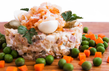 Olivier salad with shrimp, pickled cucumber, egg, decor of boiled carrots and peas on a wooden tray, board, dish, background
