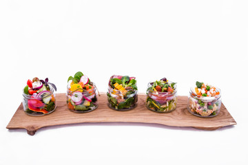 Salads in portioned jars on a wooden tray. Trendy salad in cans. The object is isolated on a white background.