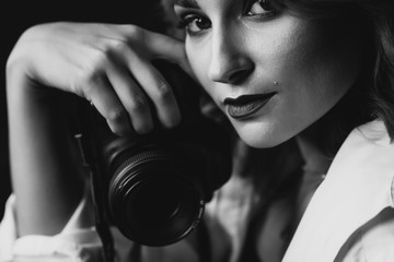 Portrait of a beautiful woman photographer with a camera in her hands in low key. Black and white art photo. Soft selective focus.