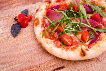 Pizza with ham, tomatoes, arugula on a wooden background. Basil leaves and tomato slices as a decoration